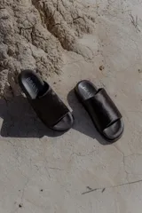 Sandalias planas negras tipo slide, con capellada ancha de pelo corto. Tienen suela de caucho expandido y base plana de 3 cm de altura.