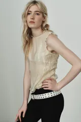 Camisa sin mangas color crema, con cuello redondo y detalle de encaje a tono en el cuello y los bordes de las sisas. Presenta un fruncido horizontal en la parte inferior y cierre con botones forrados en la espalda.