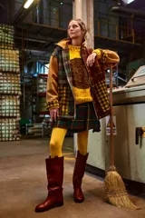 Chaqueta con cuerpo de lana a cuadros en tonos marrón, verde y amarillo. Mangas y cuello de cuero agamuzado color camel. Cierre frontal con cremallera. Falda corta a cuadros escoceses en tonos verde, rojo y azul. Medias amarillas y botas de cuero marrón. 