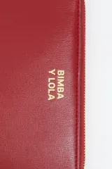 Billetera rígida de color negro con cierre de cremallera perimetral. Presenta el logo metálico de Bimba y Lola en color dorado en el frente y un tirador de cordón trenzado en tonos marrón y amarillo. El interior cuenta con compartimentos para tarjetas y un monedero con cierre.