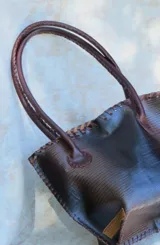 Cartera de cuero con textura crocco en color rojo, de silueta estructurada, manijas largas marrones y detalles de terminación artesanal en el borde superior.