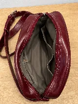 Bandolera semirrígida Sagali de cuero vacuno color bordó, con textura de cocodrilo en el bolsillo frontal y cuerpo liso. Cuenta con cierre superior y correa regulable.