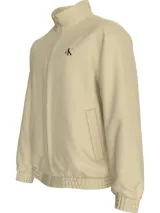 Campera de nailon estructurado color beige, con corte regular y cuello alto de canalé. Presenta cierre frontal de cremallera, bolsillos laterales, puños y bajo elásticos, y forro ligeramente acolchado. Incluye el logo de Calvin Klein bordado en el pecho.