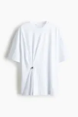 Remera de punto de algodón, corte holgado con hombros caídos y cuello redondo acanalado. Presenta un detalle metálico decorativo en un lateral que genera un efecto drapeado.