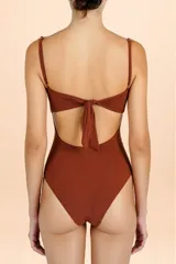 Traje de baño enterizo color terracota con diseño strapless, detalle de nudos frontales y aberturas cut-out en el torso. Incluye breteles finos ajustables.