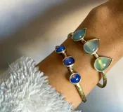 Pulsera rígida de bronce color dorado con tres piedras de ágata blancas de forma ovalada.