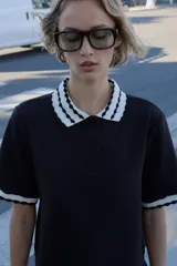 Top de tejido negro con cuello polo y bordes de manga cortos con diseño de ondas en blanco y negro. Tiene un cierre frontal de botones.