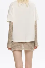 Camiseta de algodón color blanco hueso, de corte boxy y holgado, con escote redondo y mangas cortas. Presenta un pequeño logo en relieve de color rojo en el área del pecho.