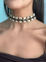 Gargantilla tipo choker trenzada, compuesta por cuentas rectangulares de acrílico con efecto marmolado en tonos marrones y blancos. Cuenta con cierre de cadena de acero quirúrgico para regular el largo.