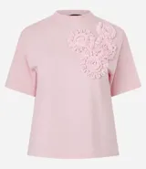 Remera blanca de algodón con cuello redondo y corte boxy, con apliques de flores de tejido en relieve en la zona del pecho.