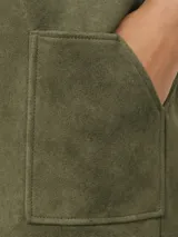 Vestido corto de corte recto y estilo minimalista, confeccionado en tela tipo gamuza negra. Presenta cuello redondo, mangas cortas y dos bolsillos frontales aplicados a la altura de la cadera.