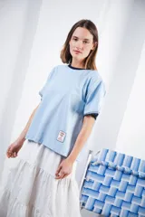 Remera de algodón color azul marino, corte relajado con hombro caído. Presenta cuello redondo blanco y bordado a mano en contraste en los puños de las mangas. Tiene un parche bordado en la parte inferior del frente.