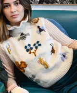 Chaleco de punto color marfil, con cuello alto estilo gorguera y bordados artesanales de insectos y elementos de la naturaleza en la parte delantera.