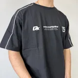 Remera oversize blanca de manga corta con detalles de líneas negras en las costuras de los hombros y mangas. Presenta un gran estampado en la espalda con el número 99 en diseño rayado y el logo de la marca en la parte superior.