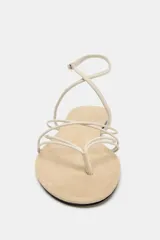 Sandalia plana de diseño minimalista con múltiples tiras finas en el empeine y cierre de pulsera con hebilla metálica en el tobillo.