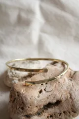 Pulsera rígida de bronce color dorado, con extremos abiertos y diseño minimalista.