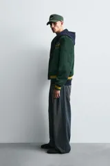 Cazadora tipo varsity de corte relajado confeccionada en tejido efecto ante color verde oscuro. Presenta cuello solapa, cierre frontal con botones a presión y puños y bajo acanalados con rayas en contraste. Incluye parches bordados en color amarillo en el frente y mangas.