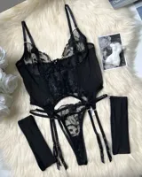 Conjunto de lencería de tres piezas color negro, compuesto por un body de encaje bordado transparente con aro y portaligas integrados, bombacha colaless a juego y medias tipo muslianas semitransparentes.