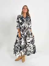 Vestido camisero midi de algodón con estampado floral en tonos rosados y blancos. Tiene cuello camisero, mangas 3/4, botones frontales, falda escalonada y cinturón fino.