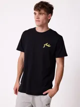 Remera de manga corta color crema con estampado gráfico en la espalda que representa un paisaje de montaña con un lago, árboles y una carpa, junto con el logo de la marca Rusty.