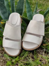 Sandalias bajas de cuero color marfil, con dos tiras anchas sobre el empeine y suela plana con detalle de costuras.