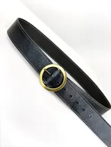 Cinto de cuero negro con textura granulada, costuras decorativas en los bordes y hebilla circular metálica en acabado plateado mate.