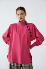 Camisa fucsia de cupro con cuello alto y cartera cruzada en delantero con abotonado de snaps soft-touch. Tiene terminación redondeada con pequeños tajos en los laterales.