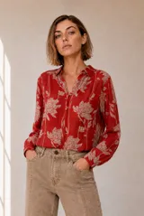 Blusa de manga larga color rojo con estampado floral en tono beige, cuello camisero y cierre frontal de botones ocultos.