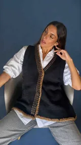 Chaleco tejido color tostado con destellos de lurex, escote en V y cierre frontal con botones. Presenta detalles de bordados y terminaciones en crochet en color crudo.