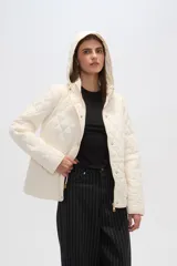 Campera acolchada de color blanco con diseño capitoneado en forma de rombos, manga larga, capucha y cierre frontal con botones a presión dorados.
