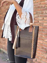 Bolso matero de cuero color chocolate con textura croco, asas cortas y detalle de costuras en los laterales. Incluye un dije con flecos en tonos beige y negro.