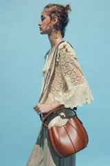 Bolso marrón con forma de saca, detalle de pespuntes en el corte y asa de mano. Incluye correa extraíble para usar como bandolera y cartera con bolsillo extraíble. Cierre con botón imantado.