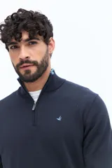 Sweater de tejido liso color verde oscuro, con cuello medio y cierre frontal parcial plateado. Presenta puños y cintura acanalados, y un pequeño logo bordado en el pecho.