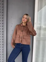 Campera corta de gamuza color marrón, con cuello clásico, cierre frontal con botones y dos bolsillos delanteros con solapa.