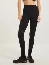 Calza deportiva negra de tiro alto, con paneles de tul transparente en la zona de los muslos y logo pequeño en la pierna.