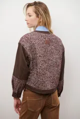Chaqueta bomber color bordó con mangas de cuero sintético marrón y cuerpo de tweed con patrón de espiga. Cierre frontal con botones a presión y cuello redondo.