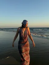 Vestido largo de silueta ajustada, con estampado abstracto en tonos azules, morados y naranjas. Presenta un escote drapeado profundo y tirantes finos.