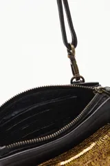 Cartera pequeña tipo bandolera de cuero vacuno negro, con detalle frontal de lentejuelas doradas. Cuenta con correa larga ajustable y extraíble, y una manija lateral corta para llevar en la muñeca.