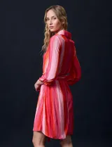 Vestido camisero midi de satén plisado con estampado a rayas verticales en tonos rosa y naranja. Tiene cuello camisero, cierre frontal con botones, mangas largas con puños abotonados y cinturón de lazo.