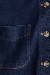Campera camisera de denim azul oscuro con cuello, cierre frontal de botones, hombros caídos, mangas largas con puños abotonados y dos bolsillos delanteros de parche.