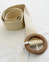 Cinturón de rafia color crudo con hebilla circular de madera clara y cierre con hebilla metálica.