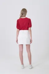 Falda mini de jean color blanco con costuras en contraste color ocre. Presenta un detalle de trenzado decorativo en los bolsillos delanteros y ruedo desflecado.