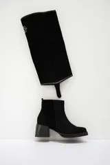 Bota de caña alta confeccionada en cuero gamuzado color marrón, con diseño de polaina desmontable que permite versatilidad en el estilo. Presenta una puntera redondeada y un taco cuadrado de altura media, ofreciendo un look clásico con un toque moderno.