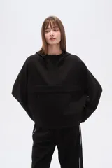 Buzo negro de corte holgado con capucha, manga larga y bolsillo frontal tipo canguro. Presenta un diseño minimalista con una solapa frontal sobre el pecho.