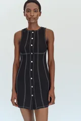 Vestido mini negro con cuello redondo y diseño sin mangas, con pespuntes en contraste y botones decorativos frontales.