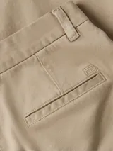 Pantalón chino color beige de corte slim, con cierre de botón y cremallera, cuatro bolsillos y logo de Tommy Hilfiger bordado en el bolsillo trasero.