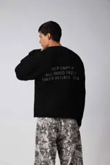 Sweater de punto acanalado con diseño de calce relajado, cuello redondo y mangas largas. Presenta una estampa gráfica pequeña en el centro del pecho y un parche con logo en el puño.