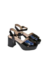 Sandalias de taco cuadrado y plataforma, confeccionadas en charol negro. Presentan tiras cruzadas en el empeine y una tira ajustable con hebilla metálica en el tobillo.