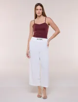 Pantalón blanco de corte wide leg corto, confeccionado en tela con textura tipo crepé, de calce relajado y caída fluida. Cuenta con cintura alta elastizada estilo pull on y un aplique de cadena metálica decorativa en el frente.
