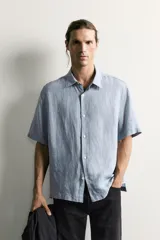 Camisa regular fit confeccionada en tejido de lino, color blanco, con cuello solapa, manga corta y cierre frontal de botonadura.